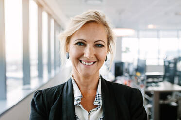 Close up portrait of successful mature businesswoman standing in office. Caucasian female executive in suit looking at camera and smiling. - JLPSF02241