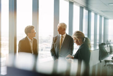Drei Geschäftskollegen, die hinter dem Glas stehen und ihre Arbeit besprechen. Ein professionelles Unternehmen, das in einem modernen Büro eine Sitzung abhält. - JLPSF02251