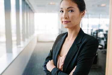 Portrait of mature businesswoman standing in office with her arms crossed. Asian female entrepreneur in suit looking at camera confidently. - JLPSF02256