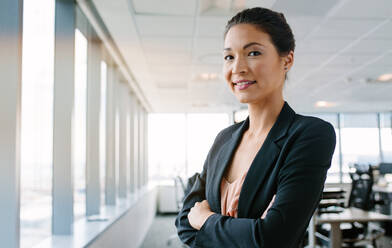 Portrait of mature businesswoman standing in office with her arms crossed and smiling. Asian female executive looking at camera confidently. - JLPSF02257