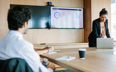 Aufnahme einer Geschäftsfrau, die in einem Konferenzraum mit Laptop neue Geschäftsideen vorstellt, während ihre Kollegen um den Tisch herum sitzen. - JLPSF02258