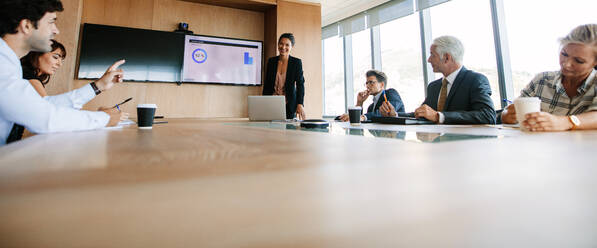 Aufnahme von Geschäftsleuten, die eine Vorstandssitzung in einem modernen Büro abhalten. Eine junge Führungskraft stellt einer Frau einige Fragen. - JLPSF02265