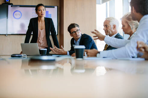 Ein Team von Geschäftsleuten, die an einem Konferenztisch zusammensitzen und diskutieren. Eine heterogene Gruppe von Geschäftsleuten trifft sich im Sitzungssaal. - JLPSF02272