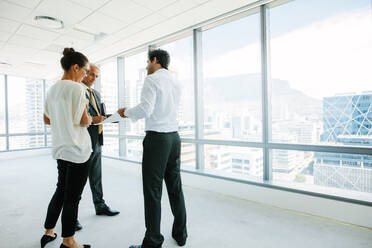 Geschäftsleute, die in einem neuen Büro stehen und mit einem Immobilienmakler diskutieren. Immobilienmakler im Gespräch mit potenziellen Kunden in einem leeren Büro. - JLPSF02289