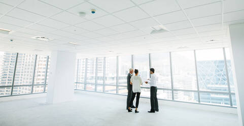 Weitwinkelaufnahme eines Immobilienmaklers mit potenziellen Kunden in einem leeren Büroraum. Ein Makler zeigt Geschäftsleuten neue Büroräume. - JLPSF02290