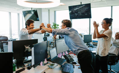 Business team cheering at good news as they congratulate each other on a success. Colleagues high fiving and clapping, celebrating success. - JLPSF02300