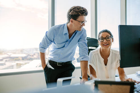 Glückliche Geschäftskollegen arbeiten zusammen an ihrem Schreibtisch. Asiatische Frau mit männlichem Kollegen in einem modernen Büro. - JLPSF02315