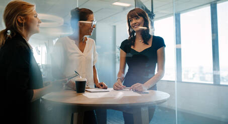 Drei weibliche Führungskräfte, die an einem Tisch stehen und diskutieren. Ein professionelles Unternehmen hat ein informelles Treffen in einem modernen Büro. - JLPSF02326