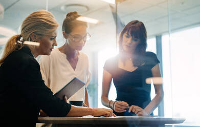 Drei Geschäftsfrauen, die am Tisch stehen und neue Projekte besprechen. Fachleute aus der Wirtschaft beim Brainstorming über neue Geschäftsideen. - JLPSF02328