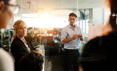 Älterer Geschäftsmann, der eine Präsentation auf einem Flipchart hält und diskutiert. Geschäftsteam während einer Strategiesitzung in einem modernen Büro. - JLPSF02352