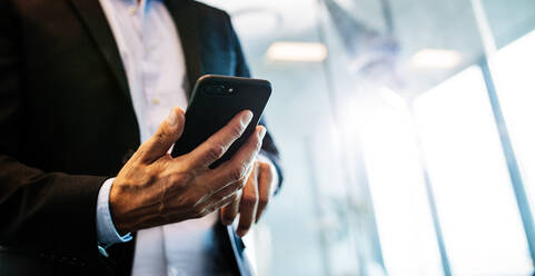 Cropped image of male entrepreneur with cell phone in office. Focus on hands of businessman with smart phone. - JLPSF02368