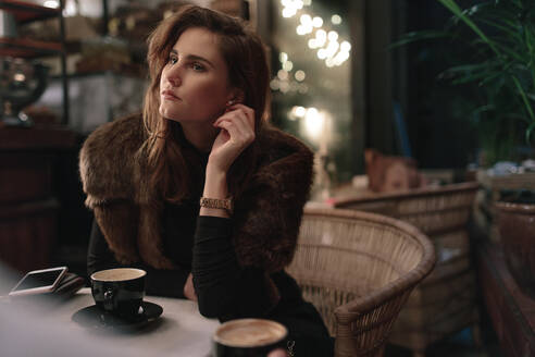 Junge attraktive Frau sitzt in einem Café und schaut weg. Nachdenkliche kaukasische Frau entspannt sich in einem Café. - JLPSF02375