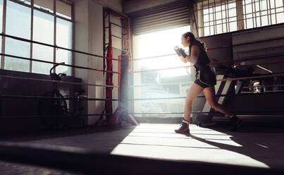 Female boxer doing shadow boxing inside a boxing ring. Boxer practicing boxing moves at a boxing studio. - JLPSF02376