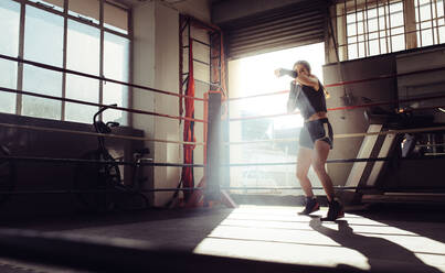 Female boxer doing shadow boxing inside a boxing ring. Boxer practicing her punches at a boxing studio. - JLPSF02377