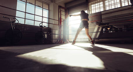 Rear view of female boxer doing shadow boxing inside a boxing ring. Boxer practicing her punches at a boxing studio. - JLPSF02378