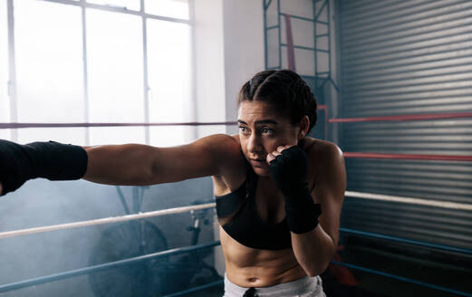 Nahaufnahme einer weiblichen Boxerin, die in einem Boxring trainiert. Eine Boxerin übt ihre Bewegungen in einem Boxstudio. - JLPSF02383