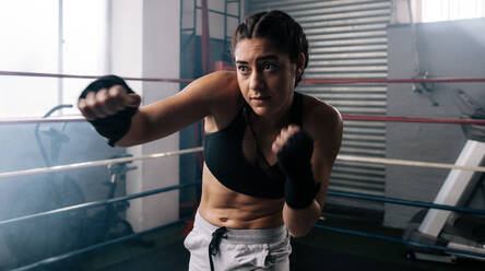 Female boxer doing shadow boxing inside a boxing ring. Boxer practicing her punches at a boxing studio. - JLPSF02384