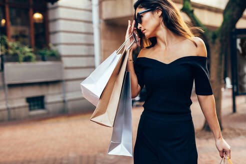 Außenaufnahme einer schönen Frau mit vielen Einkaufstaschen. Asiatisches weibliches Modell, das mit Einkaufstaschen durch die Stadt läuft. - JLPSF02386
