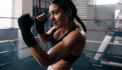 Close up of a female boxer doing shadow boxing inside a boxing ring. Boxer practicing her punches at a boxing studio. - JLPSF02389