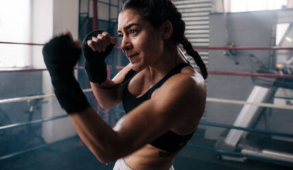 Nahaufnahme einer weiblichen Boxerin beim Schattenboxen in einem Boxring. Eine Boxerin übt ihre Schläge in einem Boxstudio. - JLPSF02389