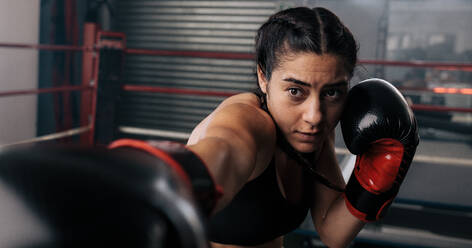 Close up of a female boxer doing shadow boxing inside a boxing ring. Boxer practicing her punches at a boxing studio. - JLPSF02393