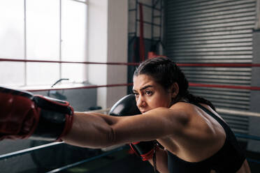 Boxer practicing her punches at a boxing studio. Close up of a female boxer doing shadow boxing inside a boxing ring. - JLPSF02398