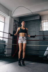 Weibliche Boxerin beim Aufwärmen in einem Boxring. Frau beim Training mit einem Springseil. - JLPSF02402