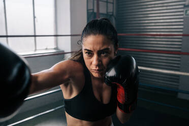 Eine Boxerin übt ihre Schläge in einem Boxstudio. Nahaufnahme einer weiblichen Boxerin, die mit ihrem Boxhandschuh in einem Boxring schlägt. - JLPSF02412