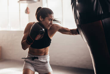 Female boxer hitting a huge punching bag at a boxing studio. Woman boxer training hard. - JLPSF02416