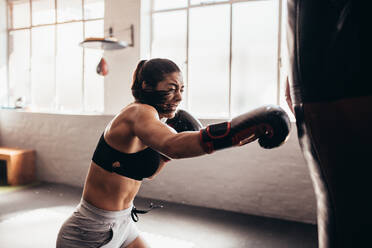 Weiblicher Boxer, der in einem Boxstudio auf einen riesigen Sandsack schlägt. - JLPSF02418