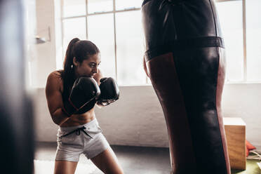 Female boxer hitting a huge punching bag at a boxing studio. Woman boxer training hard. - JLPSF02419