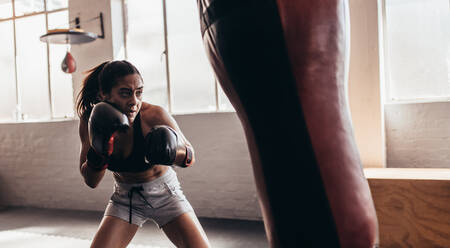 Female boxer hitting a huge punching bag at a boxing studio. Woman boxer training hard. - JLPSF02420