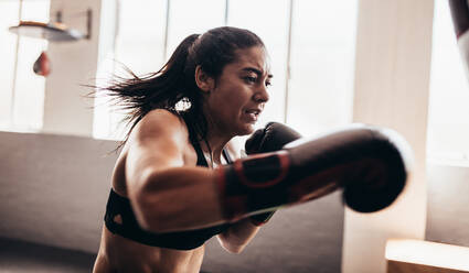 Eine Boxerin übt ihre Schläge in einem Boxstudio. Nahaufnahme einer weiblichen Boxerin, die mit ihren Boxhandschuhen schlägt. - JLPSF02421
