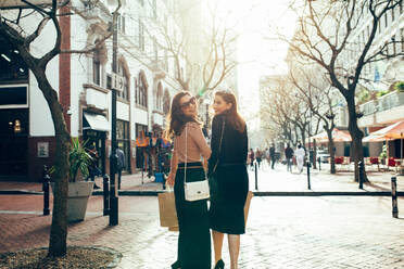 Glückliche junge Frauen mit Einkaufstüten, die eine Straße entlanglaufen. Rückansicht von Freundinnen beim Einkaufen in der Stadt. - JLPSF02424