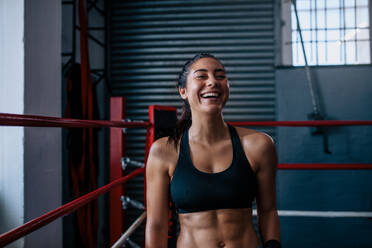Lächelnde Boxerin, die während ihres Trainings in einer Ecke des Boxrings sitzt. Boxerin beim Training in einem Boxstudio. - JLPSF02432