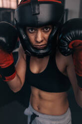 Close up portrait of a female boxer in her boxing gear. Woman boxer at a boxing studio wearing head guard and boxing gloves. - JLPSF02435