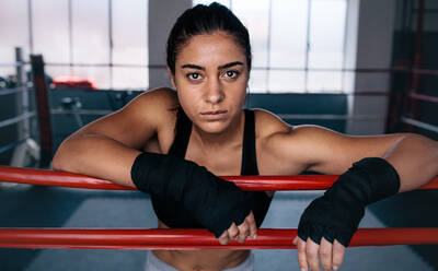 Nahaufnahme einer weiblichen Boxerin, die in einem Boxring steht und ihre Arme auf das Seil des Boxrings stützt. - JLPSF02438