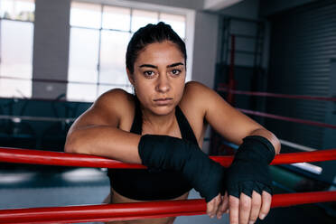 Eine weibliche Boxerin steht in einem Boxring und stützt ihre Arme auf das Seil des Boxrings. - JLPSF02439
