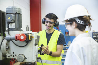 Smiling mechanic with protective eyewear working by coworker in workshop - PCLF00024