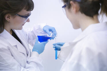 Scientist pouring chemical in test tube for experimenting by coworker at laboratory - PCLF00033