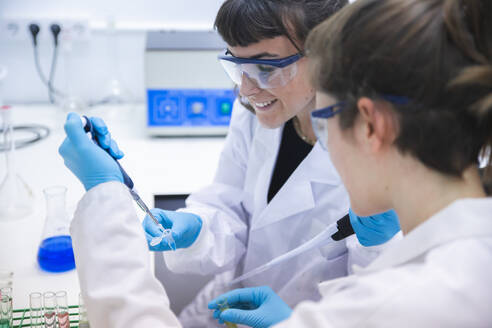 Lächelnder Wissenschaftler, der eine Pipette zum Experimentieren mit einem Kollegen im Labor benutzt - PCLF00037