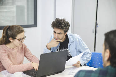 Geschäftsfrau, die einen Laptop benutzt und sich mit einem Kollegen im Büro unterhält - PCLF00044