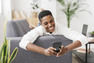 Lächelnde Frau, die auf der Couch liegt und ein Mobiltelefon benutzt - JCZF01127