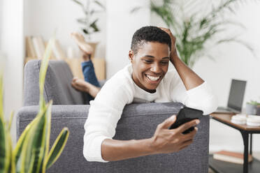 Smiling woman lying on couch using mobile phone - JCZF01129