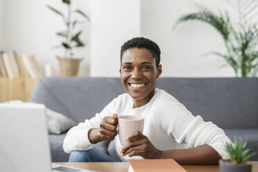 Porträt einer lächelnden Frau, die eine Tasse Kaffee in einem liebevollen Zimmer zu Hause hält - JCZF01137