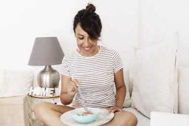 Smiling woman having breakfast in living room at home - RFTF00307