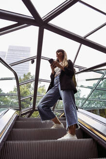 Frau mit Smartphone auf Rolltreppe stehend - VEGF05982