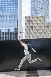 Man with backpack jumping in front of buildings - VEGF05984