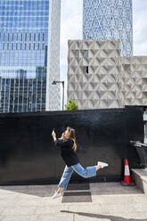 Glückliche Frau mit Smartphone, die an einem sonnigen Tag vor einem Gebäude springt - VEGF05987