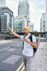 Man with disposable coffee cup hailing ride on road in city - VEGF05994